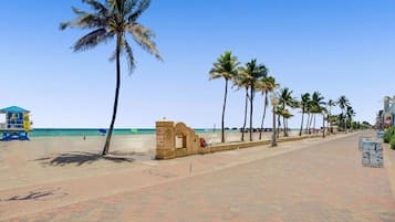 A beachside promenade with palm trees, a lifeguard tower, and a clear view of the ocean.