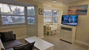 En moderne stue med sofa, sofabord, fjernsyn og spiseområde med bord og stole.