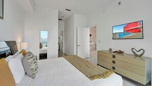 A bedroom with a bed, a dresser, a TV, and a view of a cityscape.