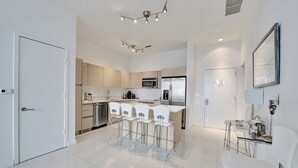 A modern kitchen with a central island, stainless steel appliances, and a dining area with white chairs.