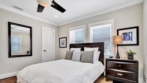 A bedroom with a large bed, a ceiling fan, a nightstand, and a window with blinds.