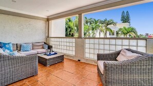 A balcony with wicker furniture, a tiled floor, and a view of palm trees and buildings.