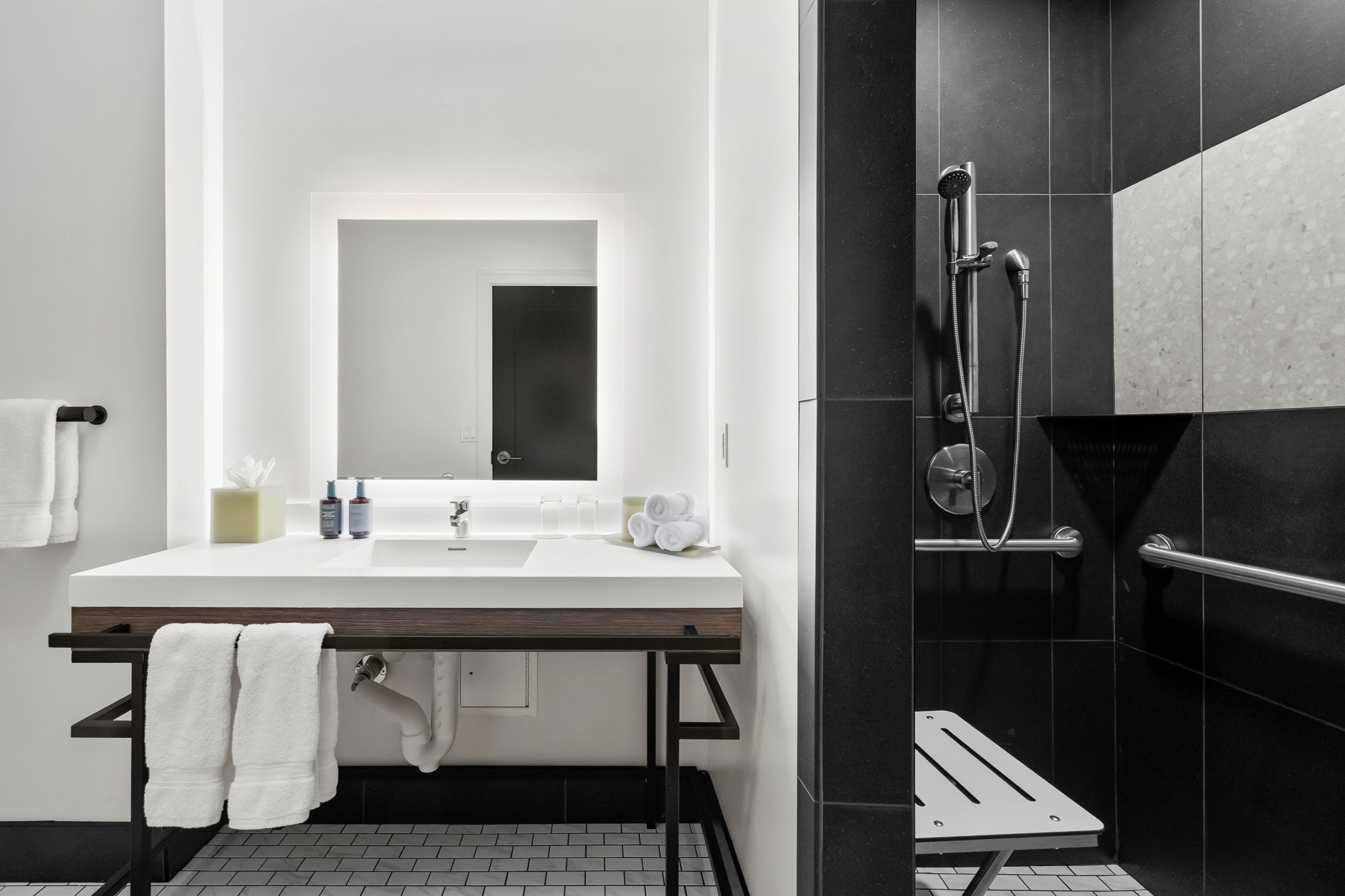 Un baño moderno con lavamanos blanco, espejo y zona de ducha con azulejos negros.