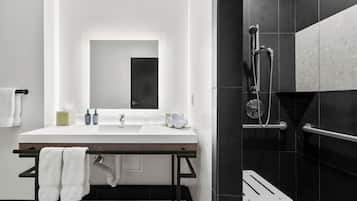 Un baño moderno con lavamanos blanco, espejo y zona de ducha con azulejos negros.