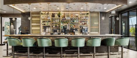 A bar area with a central counter, multiple shelves of bottles, and green bar stools.