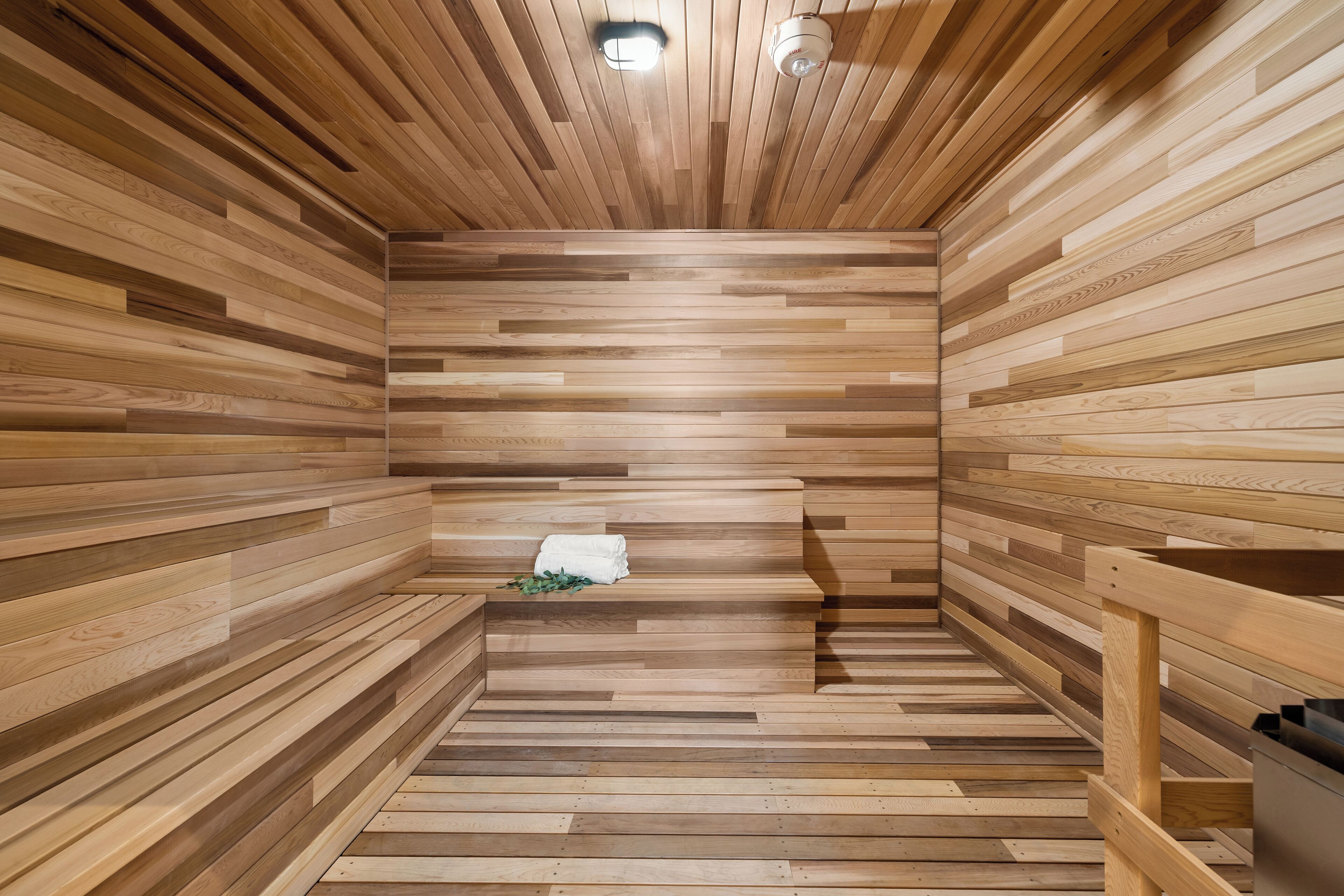 A sauna with wooden slats on the walls and floor, a bench, and a towel on the bench.