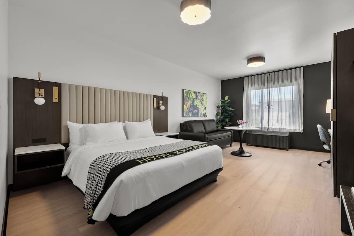 A modern hotel room with a large bed, a desk, a sofa, and a window with curtains.