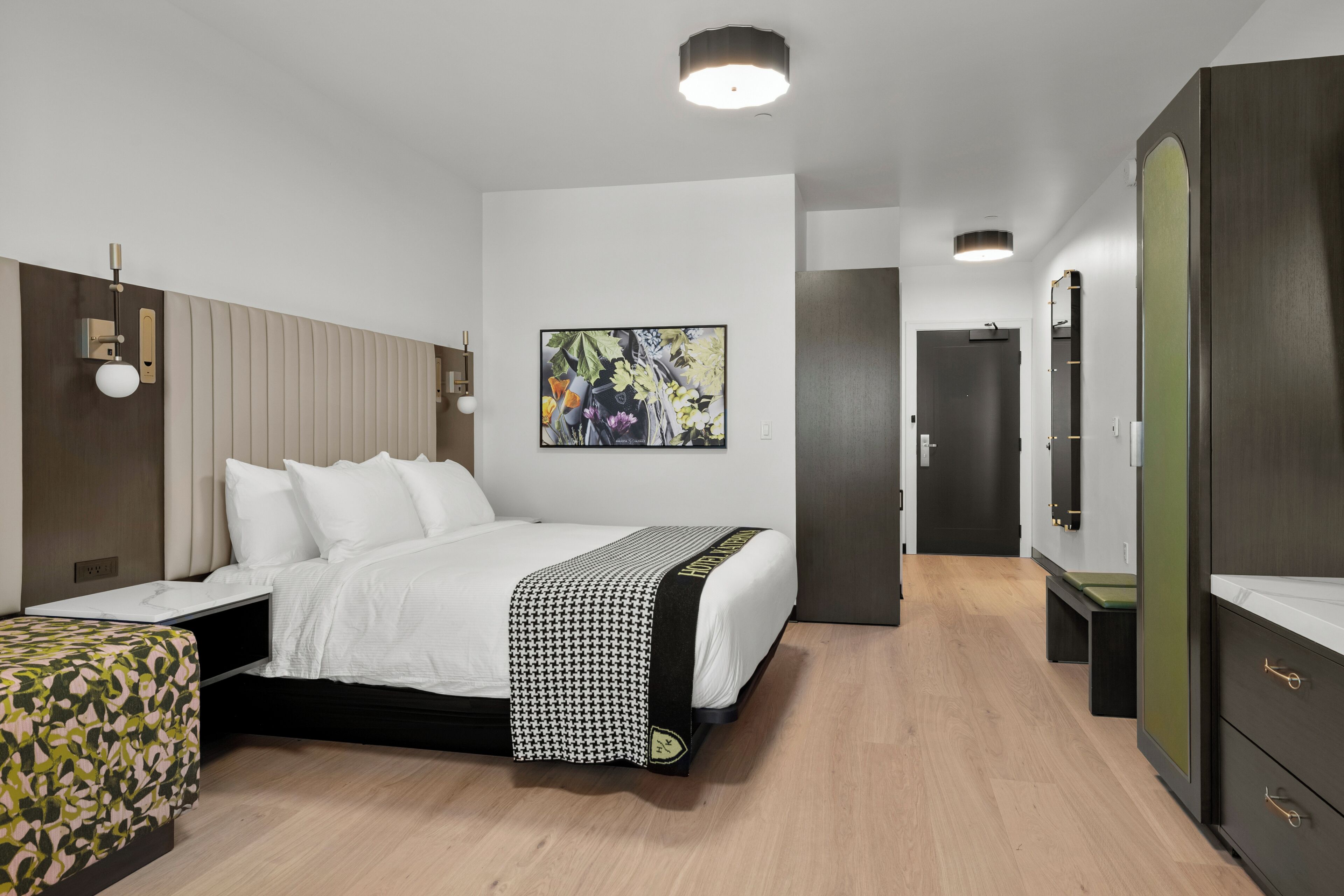 A modern hotel room with a bed, a bedside table, a wardrobe, and a painting on the wall.