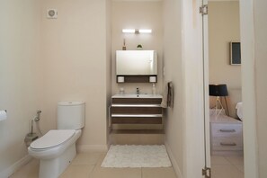Ein modernes Badezimmer mit Toilette, Waschbecken und Spiegel. Auf dem Boden liegt ein weißer Teppich und eine kleine Ablage mit Pflegeprodukten.