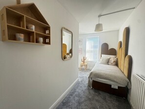 A bedroom with a bed, a wooden shelf, a mirror, and a window.