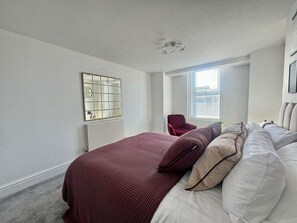 A bedroom with a bed, a chair, a radiator, and a window.