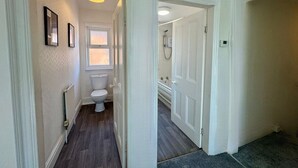 A hallway leading to a bathroom with a toilet, a shower, and a bathtub.