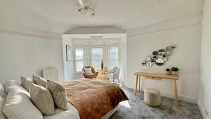A bedroom with a bed, a desk, and a chair. There is a window with blinds and a radiator.