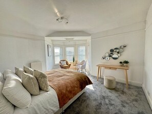 Un dormitorio con cama, escritorio y silla. Hay una ventana con persianas y un radiador.
