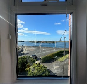 A view through a window with a clear sky, a body of water, and a road with vehicles.