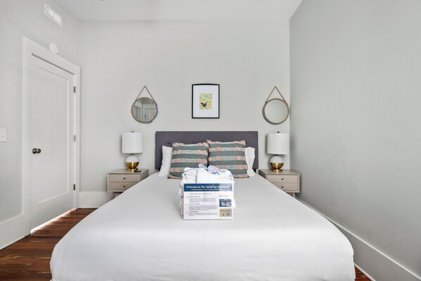 Une chambre d’hôtel avec un grand lit, deux tables de chevet avec des lampes, une porte et un tableau encadré au mur.