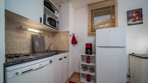 A compact kitchen with a built-in stove, microwave, and refrigerator. There are shelves with kitchenware and a red rug on the floor. - Studio in Allos with Stunning Mountain Views (Allos)