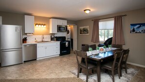 A compact kitchen with white cabinets, a microwave, a dishwasher, and a refrigerator. There is a dining table with chairs and a rug in the center.