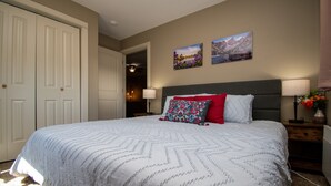 A bedroom with a large bed, a nightstand with a lamp, and two wall-mounted paintings.
