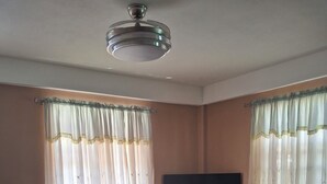 Un soggiorno con televisore a schermo piatto su un supporto in legno, due poltrone, un tappeto decorato e una ventola a soffitto.