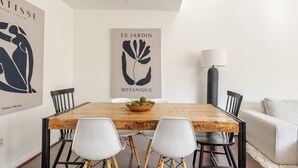 A dining area with a wooden table, white chairs, and a bowl of fruit. There are two framed artworks on the wall, one titled "Abstract Collection" and the other "Le Jardin Botanique". - A Modern & Cozy Townhome with good vibes (Houston)