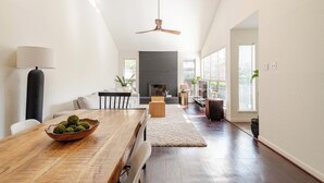 A spacious dining area with a wooden table, chairs, and a bowl of fruit. A fireplace is visible in the background, and there is a ceiling fan above. - A Modern & Cozy Townhome with good vibes (Houston)
