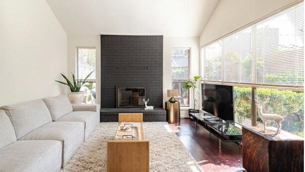 A modern living room with a fireplace, a sofa, a coffee table, a TV, and a large window with blinds. - A Modern & Cozy Townhome with good vibes (Houston)