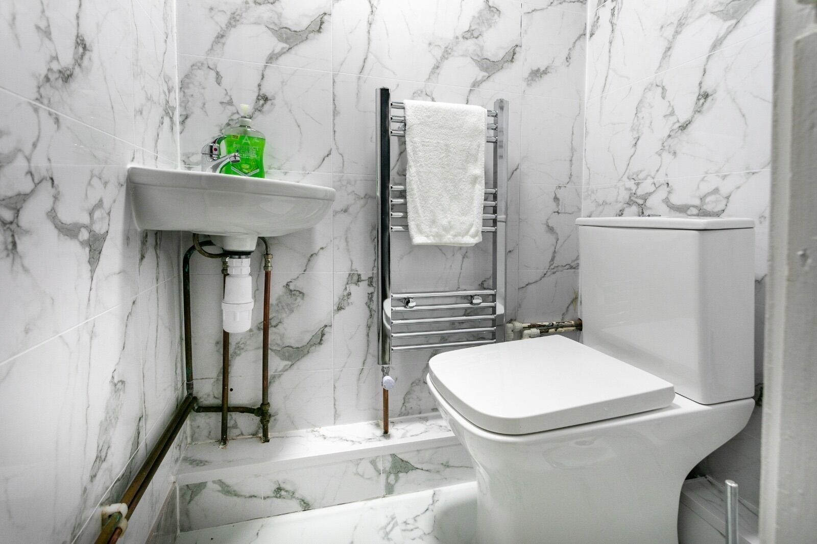 A bathroom with a white toilet, a sink with a green bottle, and a towel rack.
