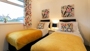 Habitació d'hotel amb dos llits, una tauleta de nit, una làmpada i una finestra amb cortines.