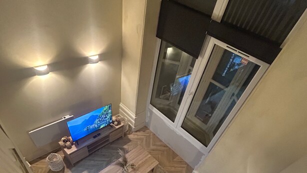 A high-ceilinged room with a television, a small wooden table, and a bench. - Apartment - Parking - Pet Friendly - City Centre (Leeds)