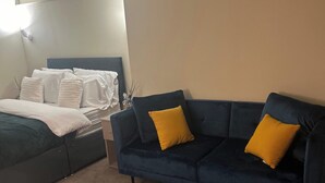 A bedroom with a bed, a dark blue sofa with yellow cushions, and a nightstand. - Apartment - Parking - Pet Friendly - City Centre (Leeds)