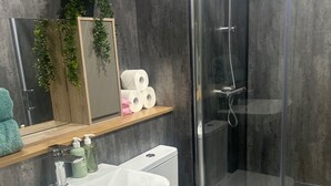 A modern bathroom with a white sink, two toilets, a glass shower enclosure, and a wooden shelf with toiletries. - Apartment - Parking - Pet Friendly - City Centre (Leeds)