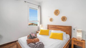 A hotel room with a wooden bed, white bedding, and a window with a view. - Stunning Pool Villa – Treasure of the Bay (La Trinité)