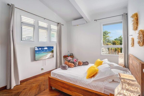 A bedroom with a wooden bed, a TV mounted on the wall, and a window with curtains.