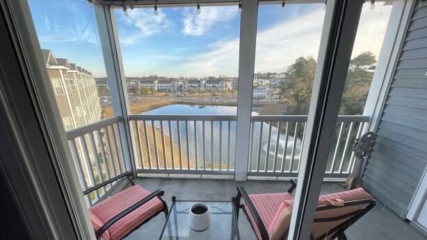 A balcony with a glass table and two chairs, overlooking a body of water and buildings. - 3-bedroom condo in superb Little River with AC, WiFi (Little River)