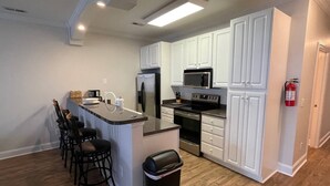 A modern kitchen with white cabinets, stainless steel appliances, a central island with bar stools, and a fire extinguisher mounted on the wall. - 3-bedroom condo in superb Little River with AC, WiFi (Little River)