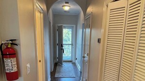 A hallway with wooden flooring, white walls, and a fire extinguisher mounted on the wall. - 3-bedroom condo in superb Little River with AC, WiFi (Little River)