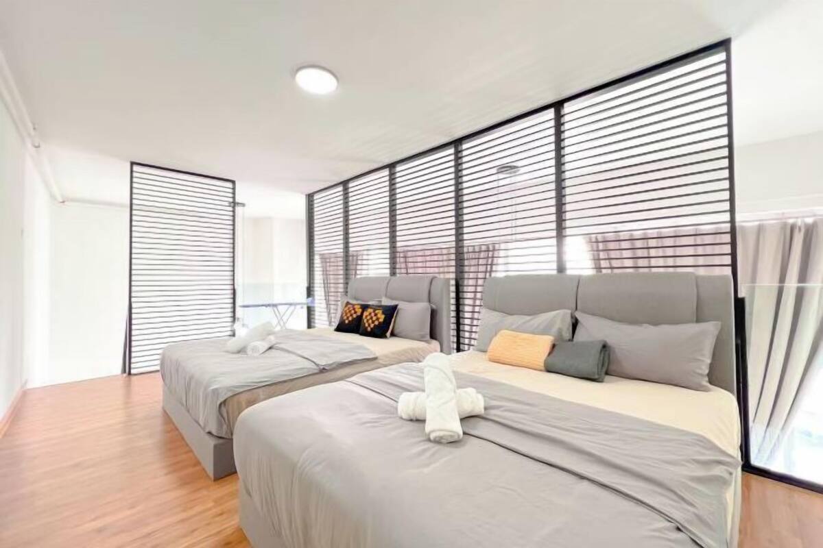 A modern hotel room with two beds, a large window with blinds, and a wooden floor.