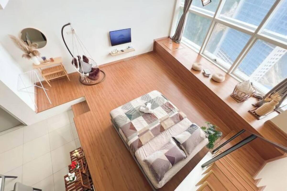 A modern room with a bed, a hanging chair, a TV, and a large window with a city view.