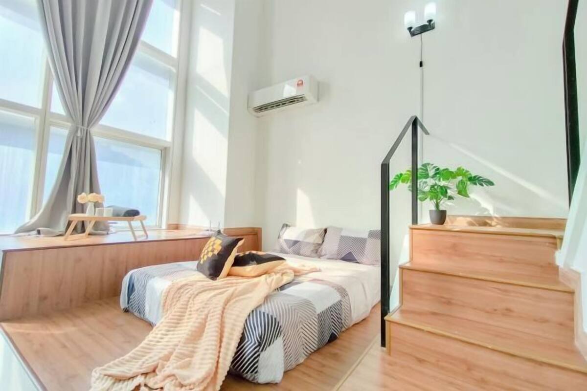 A bedroom with a bed, a desk, a staircase, and a potted plant.