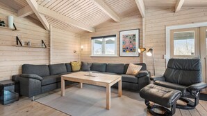 Un salon chaleureux avec un plafond en bois, un canapé gris, un fauteuil en cuir noir, une table basse en bois et un tapis.