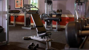 Ein Fitnessraum mit Trainingsgeräten, darunter eine Bank und Kurzhanteln.