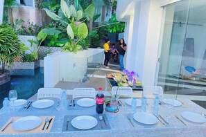 An outdoor dining area with tables set for a meal, surrounded by greenery and a pool. - Samui Sky Pool Villa (Koh Samui)
