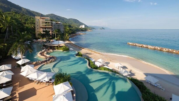 A resort with a swimming pool, beach, and mountain backdrop.