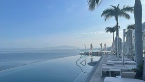An infinity pool with a view of the sea, lounge chairs, and palm trees.