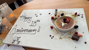 A dessert table with a cake and a message card that reads "Happy 18th Anniversary!!".