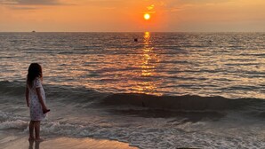 A sunset over the ocean with a person standing on the shore.