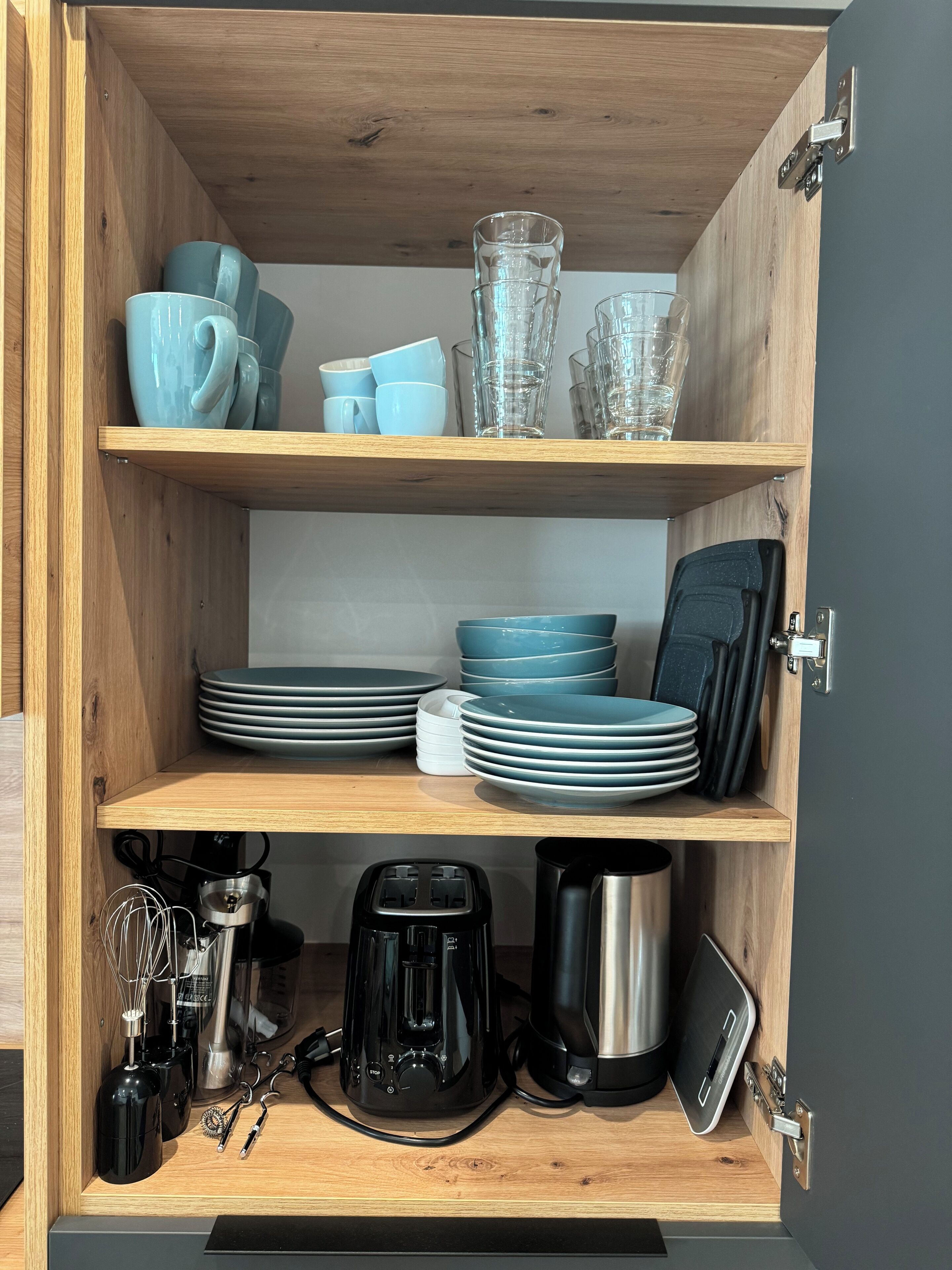 Un armario de cocina con repisas que contienen platos, tazones, tazas y vasos.