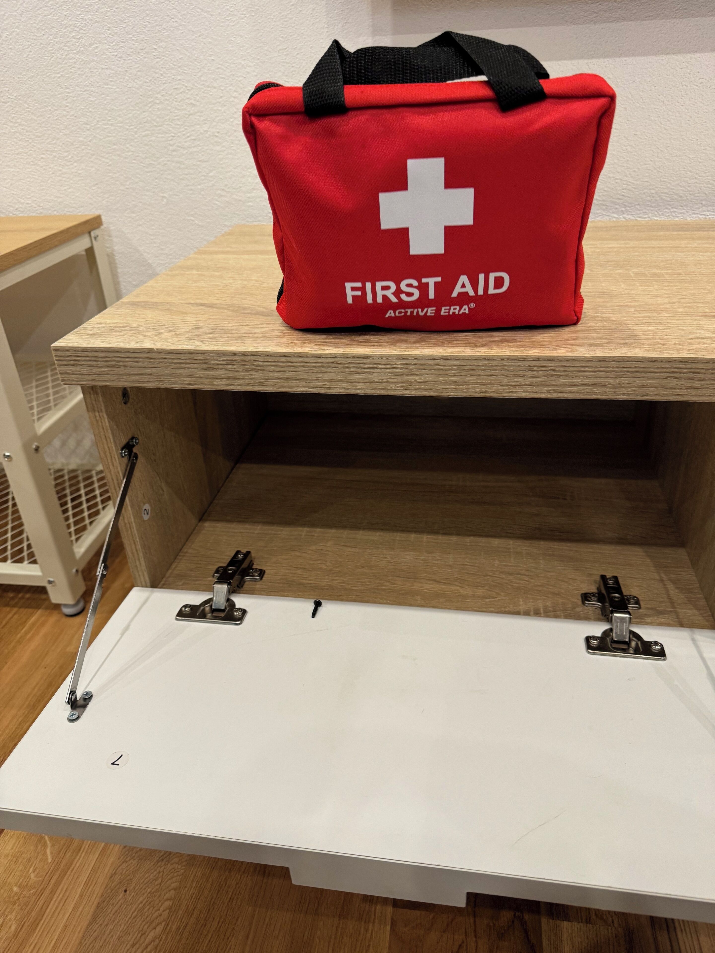 A red first aid bag labeled "FIRST AID ACTIVE ERA" on a wooden shelf.