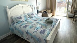 A bedroom with a bed, a nightstand, a sofa, and a view of the outside.